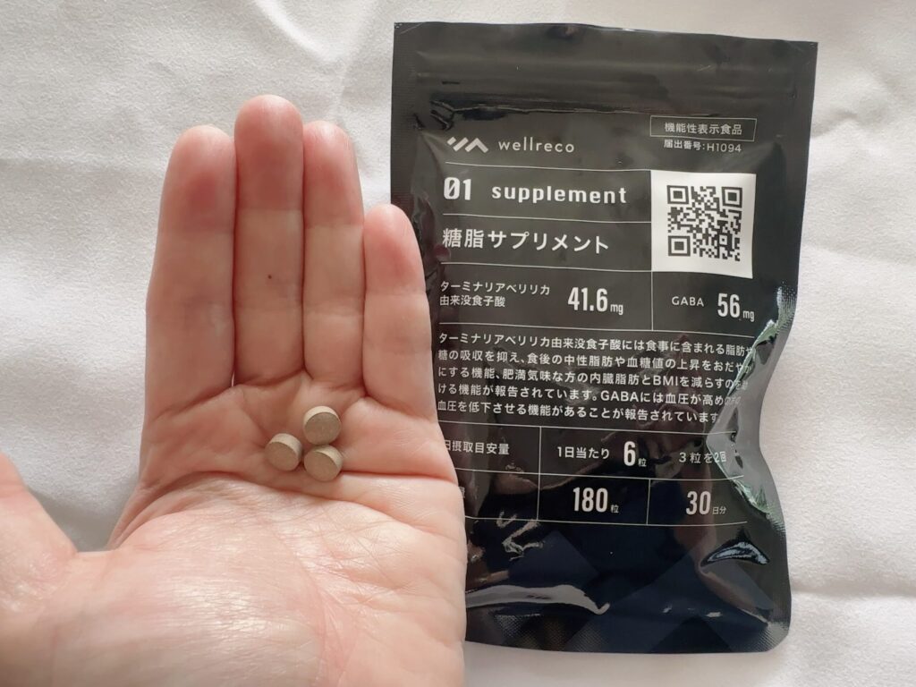 ウェルレコ糖脂サプリ1回分3粒を手のひらに乗せてパッケージと並べた写真