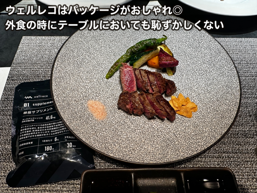 ウェルレコの糖脂サプリメントを外食時のテーブルに置いた様子。ステーキ料理の横に黒いシンプルなパッケージがあり、「ウェルレコはパッケージがおしゃれ◎外食の時にテーブルにおいても恥ずかしくない」と表示された画像